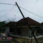 Terlihat tiang jaringan listrik hampir roboh ke rumah warga.