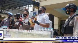 Caption: Kapolsek Tambaksari didampingi Kanit Reskrim tunjukkan puluhan botol miras dari hasil razia.