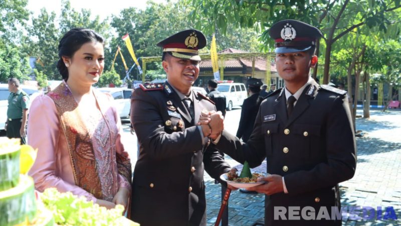 Caption: didampingi istri, Kapolres Bangkalan AKBP Hendro Sukmono berikan potongan tumpeng kepada anggotanya saat momen Hari Bhayangkara ke-79. 