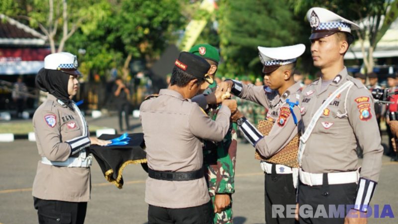 Caption: Kapolres Sampang AKBP Hartono pasang pita kepada personel TNI, saat apel Operasi Patuh Semeru 2025, (sumber foto: Humas Polres Sampang). 