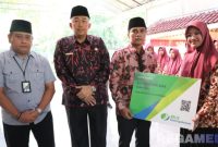 Caption: Bupati Bangkalan Lukman Hakim, menyerahkan secara simbolis kartu peserta BPJS Ketenagakerjaan kepada perwakilan peserta Kafilah MTQ, (foto istimewa). 